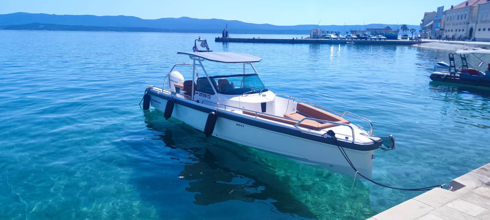 Axopar 28 T-Top liegt am Steindock im klaren Hafen mit dalmatinischen Bergen dahinter – Avangard Charter-Bootsverleih Trogir Kroatien