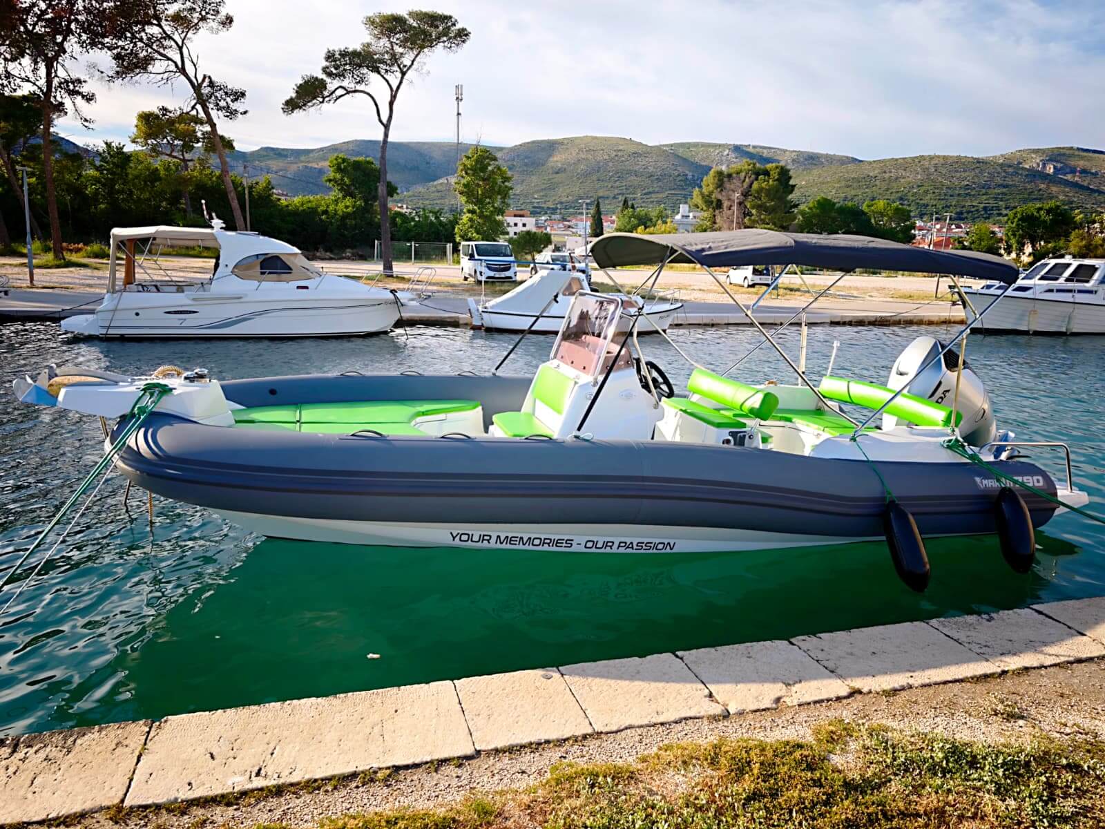 Seitenansicht der Marlin 790 mit dem Slogan YOUR MEMORIES OUR PASSION vor Anker im türkisfarbenen Hafen – Avangard Charter-Bootsverleih Trogir